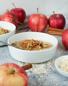 Zusehen ist ein veganes Apfel Porridge mit Zimt und Walnüssen in einer Porzellanschale|Auf dem Bild ist ein Apfel Zimt Porridge mit Nüssen zu sehen||Hier sieht man ein veganes Apfel Porridge mit Walnusskernen und gebratenen Apfel