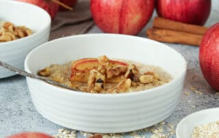 Zusehen ist ein veganes Apfel Porridge mit Zimt und Walnüssen in einer Porzellanschale